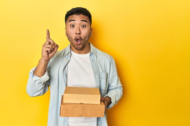 Photo asian man holding delivery food boxes yellow studio backdrop having some great idea