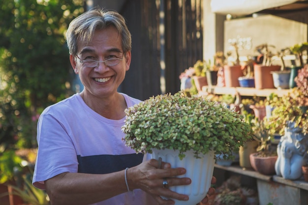Foto uomo asiatico che tiene vaso per piante da casa e sorridente a trentadue denti con felicità