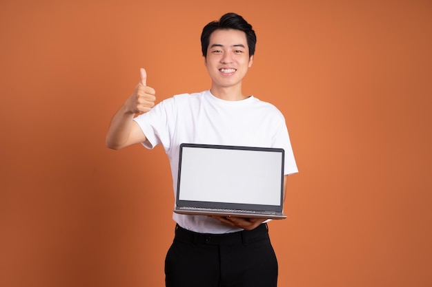 Asian man holding laptop isolated on orange background