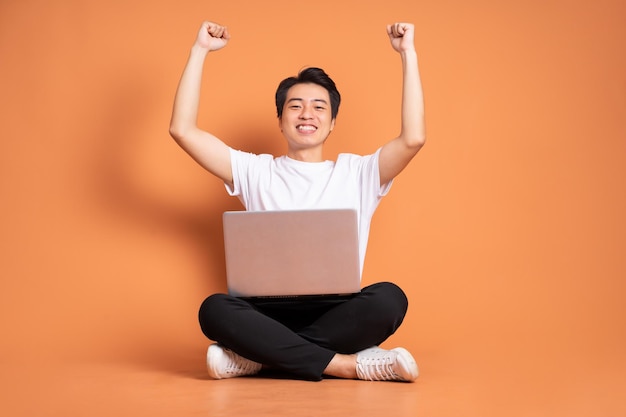 Asian man holding laptop isolated on orange background