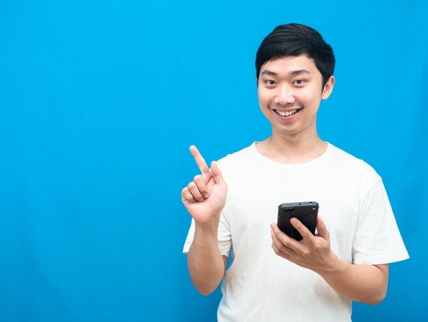 Asian man holding mobile phone happy smile and point finger at copy space blue background