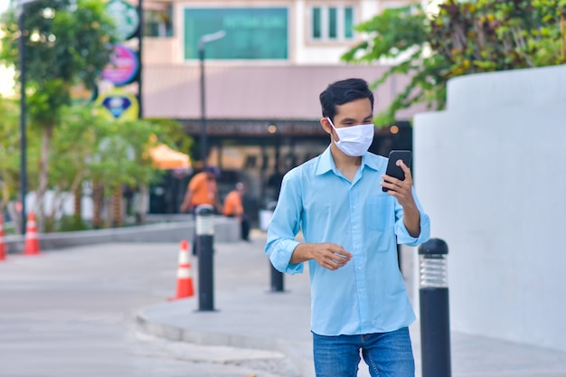모바일 스마트 폰 사용 얼굴 마스크를 들고 아시아 남자 코로나 바이러스 PM2.5 거리 새로운 정상적인 사회적 거리에 걸어 보호