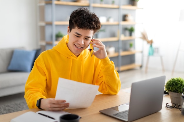 Asian man holding paper reading report talking on phone