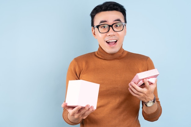 Азиатский мужчина держит розовую подарочную коробку на синем фоне