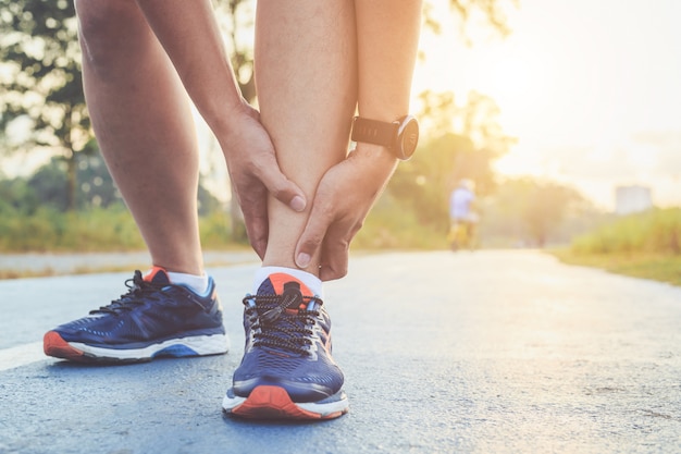 Asian man holds on his ankle while running on road in the park