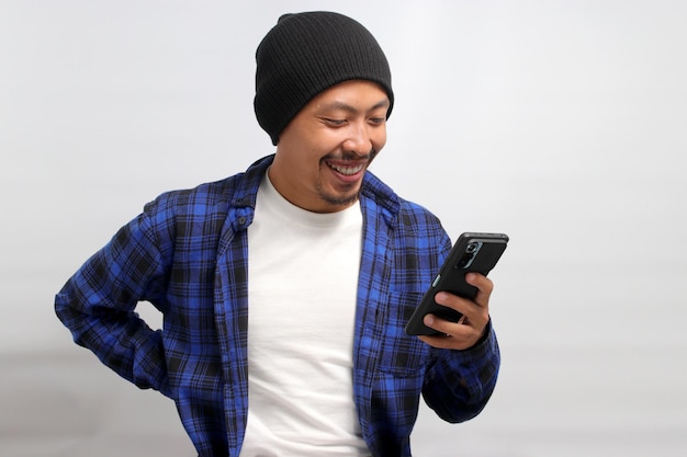 Asian man holds his smartphone displaying a joyful smile while standing against a white background