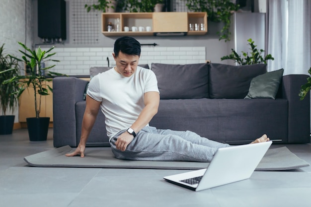 Asian man at home engaged in fitness online uses laptop for joint activities active lifestyle