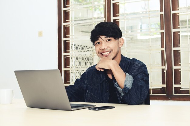 The Asian man is sitting in front of the laptop with a happy expression