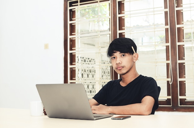 The Asian man is sitting in front of the laptop with a serious expression