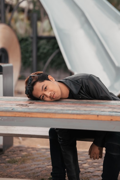 An Asian man is sitting on a wooden chair while wearing a black leather shirt and jacket