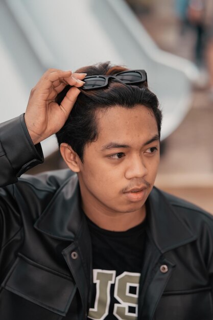 An Asian man is sitting on a wooden chair while wearing a black leather shirt and jacket