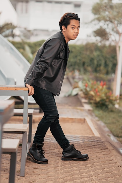 An Asian man is standing beside a cafe table in black leather clothes