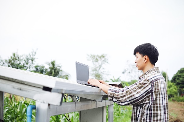 아시아 남자가 노트북을 사용하여 태양 전지 교체 전원 시스템을 확인하고 있습니다. 녹색 에너지 작업 기술 혁신