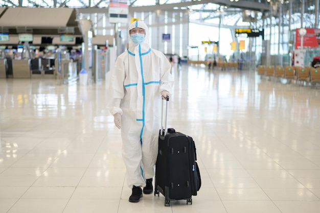 Un uomo asiatico indossa una tuta ppe in aeroporto internazionale, viaggi di sicurezza, protezione covid-19, concetto di allontanamento sociale