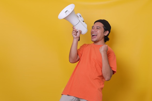 Asian man over isolated yellow wall shouting through a megaphone while celebrating success Yes man