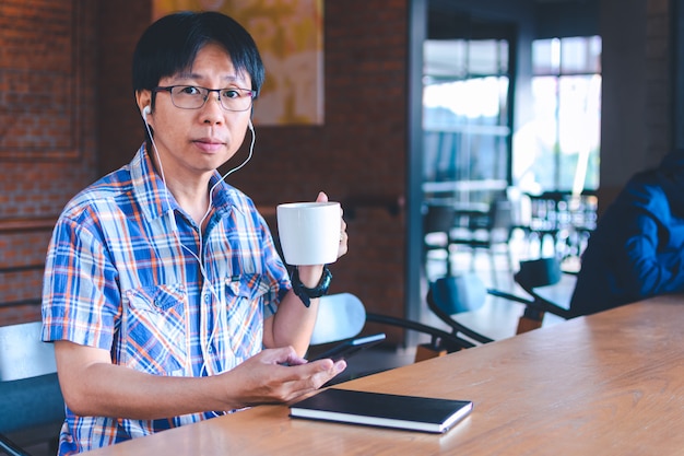 Азиатский человек слушает музыку и читает в кафе