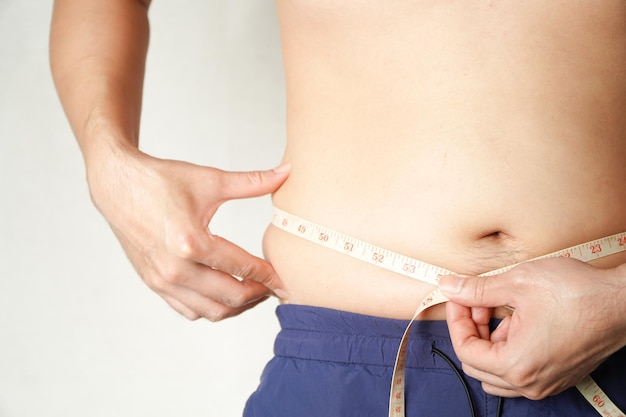 Asian man measuring belly fat with tape measure on a white background