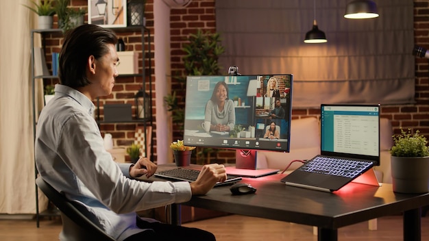 Uomo asiatico che incontra uomini d'affari in videochiamata remota, utilizzando la connessione della webcam per le telecomunicazioni. partecipazione alla chat di videoconferenza online con un gruppo di colleghi. .