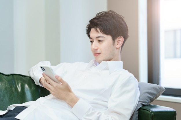 Asian man operating a smartphone while relaxing on the sofa