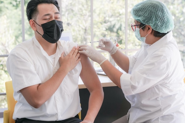 Asian man people giving his arm to nurse for injection vaccination at hospital during pandemic. Medical Vaccination for Essential people social life.Vaccine and covid-19 outbreak.