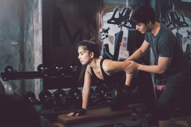 Foto personal trainer uomo asiatico con manubri attrezzature per esercizi con donna asiatica in palestra