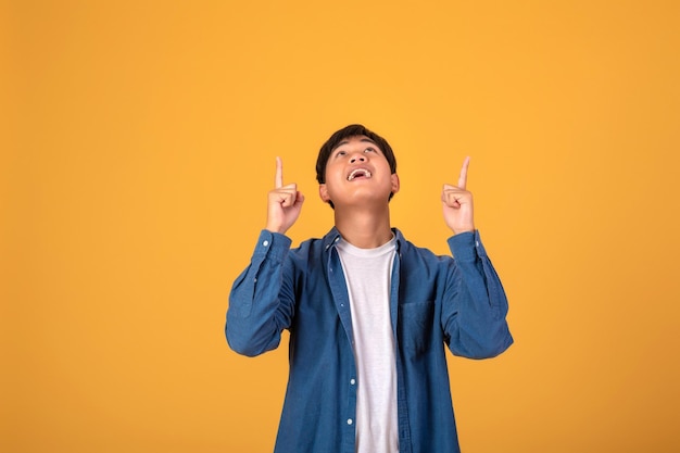 Asian man pointing his finger to look up On orange background