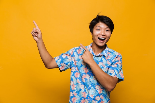 Asian man posing isolated over yellow space pointing.