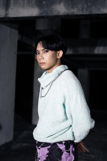 An asian man posing in a white sweater and a chain necklace around his neck