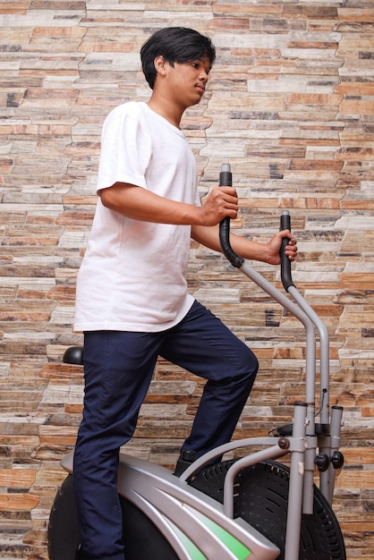 Asian man practicing sport with the exercise bike at home