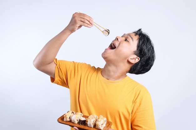 Foto uomo asiatico alza la mano e mangia sushi con le bacchette su sfondo bianco