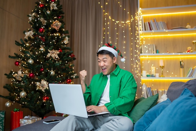 Asian man reading happy news on laptop at home for christmas\
businessman working remotely during new