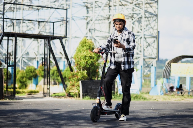 電話を見ながら電動スクーターに乗るアジア人男性。近代的で生態学的な輸送c