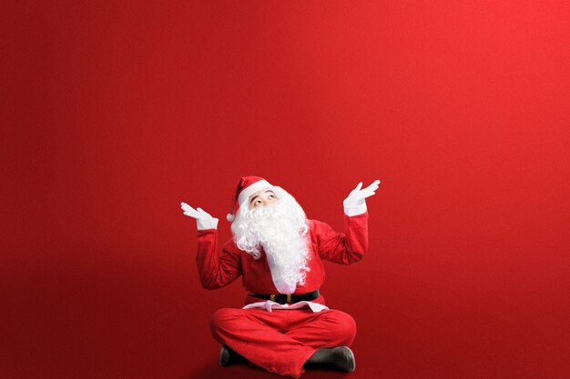 Asian man in Santa costume with open palm gesture sitting with a colored.