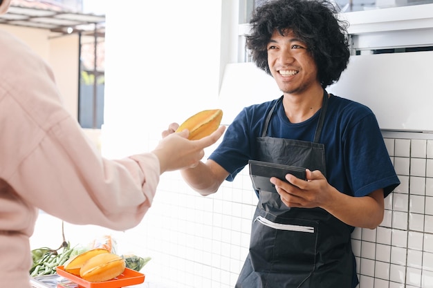 Asian man seller wear apron serves the customer who buy his fruit