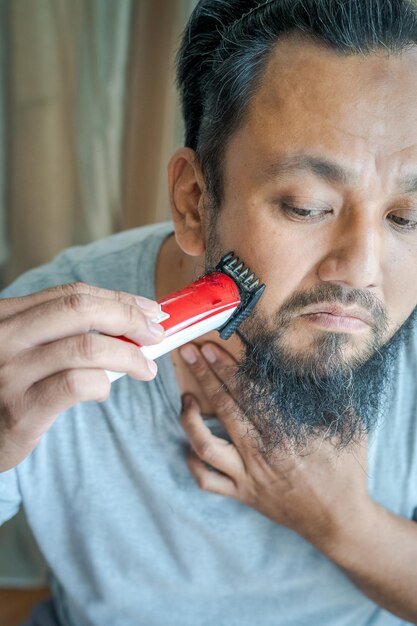 Foto uomo asiatico che si rade la barba con una macchina da rasoio elettrica vista ad alto angolo