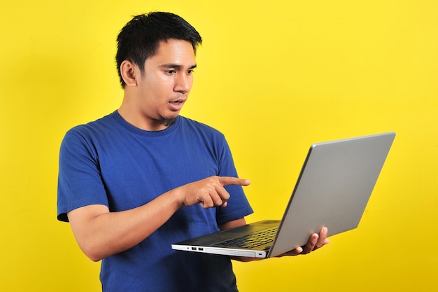 Asian man shocked what he see in the laptop, isolated on yellow background