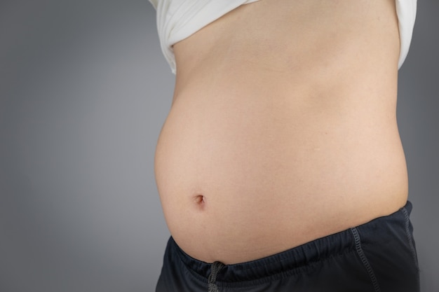 Азиатский мужчина показывает живот, что лишний вес вреден для здоровья и рискует заболеть.