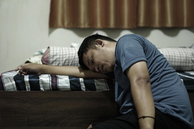 泣いている寝室に座っているアジア人男性