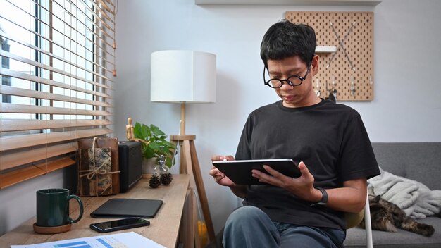 거실에 앉아 디지털 태블릿으로 작업하는 아시아 남자