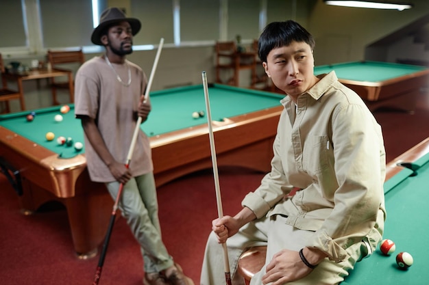 Asian man sitting on pool table in club