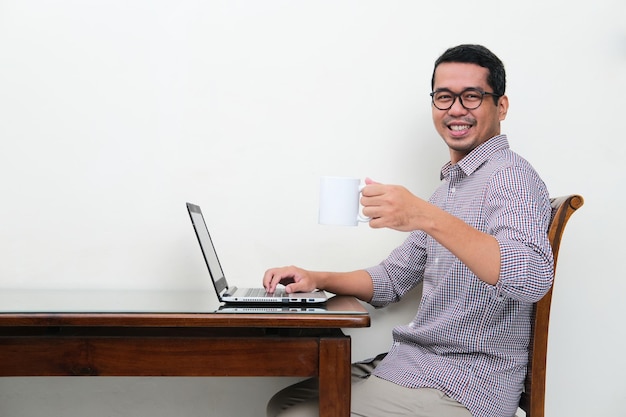 Asian man smiling to camera when working using laptop