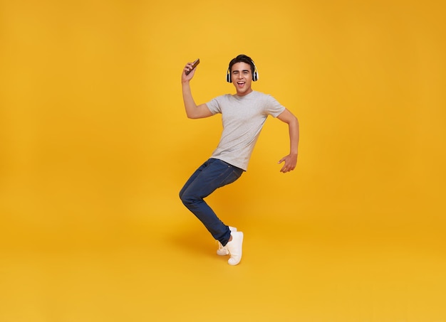 Asian man smiling holding smartphone and jumping wearing wireless headphone listening to music