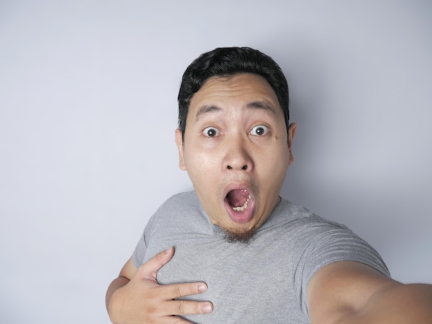 Asian man smiling while taking selfie photograph of himself on his smart phone with funny expression