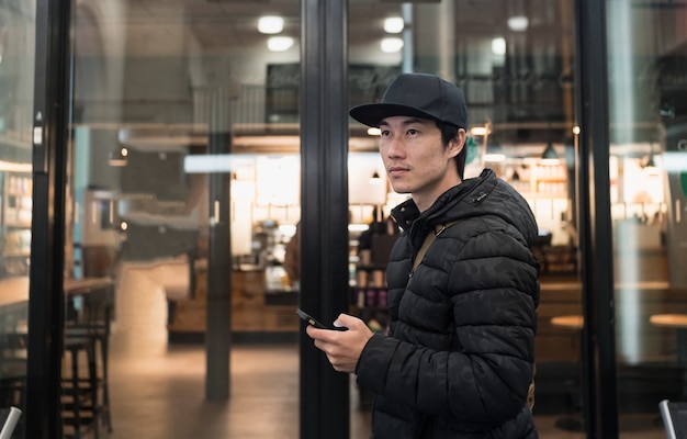 Asian man stand and holding smartphone by cafe