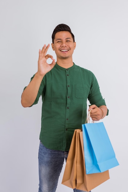 Foto uomo asiatico in piedi con un gesto della mano oke mentre porta le borse della spesa