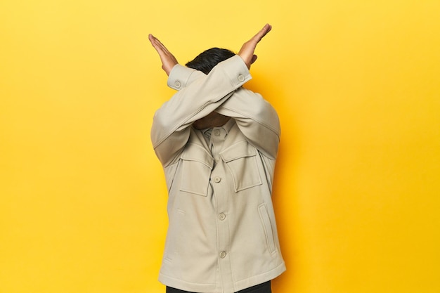 Asian man in stylish gray shirt on yellow studio keeping two arms crossed denial concept