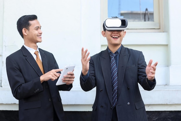 VR メガネとタブレット スマートフォンを使用してスーツを着たアジア人男性、外でデジタル デバイス技術を設定