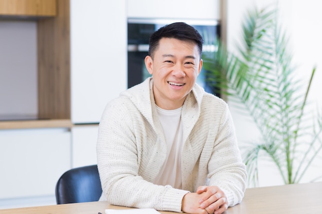 asian man talking online on video call at home in living room or kitchen