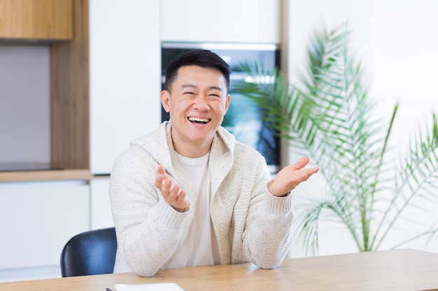 Uomo asiatico che parla online durante una videochiamata a casa con l'auricolare