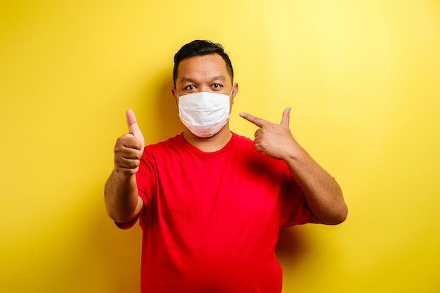 Asian man thumb up and wearing masks to prevent the spread of Corona virus against yellow background